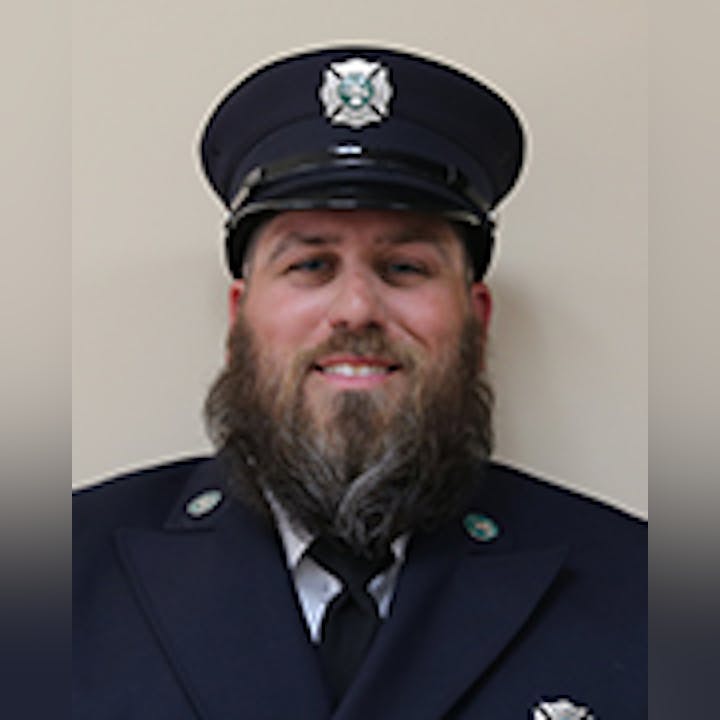 Kraig Marquart in a uniform with a cap with a badge, sporting a beard and smiling.