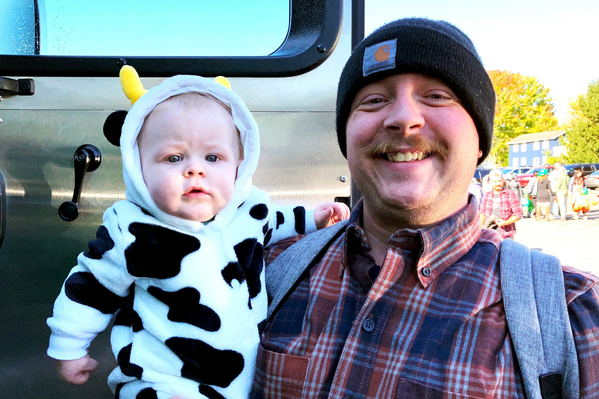 A smiling man holding a baby in a cow costume.