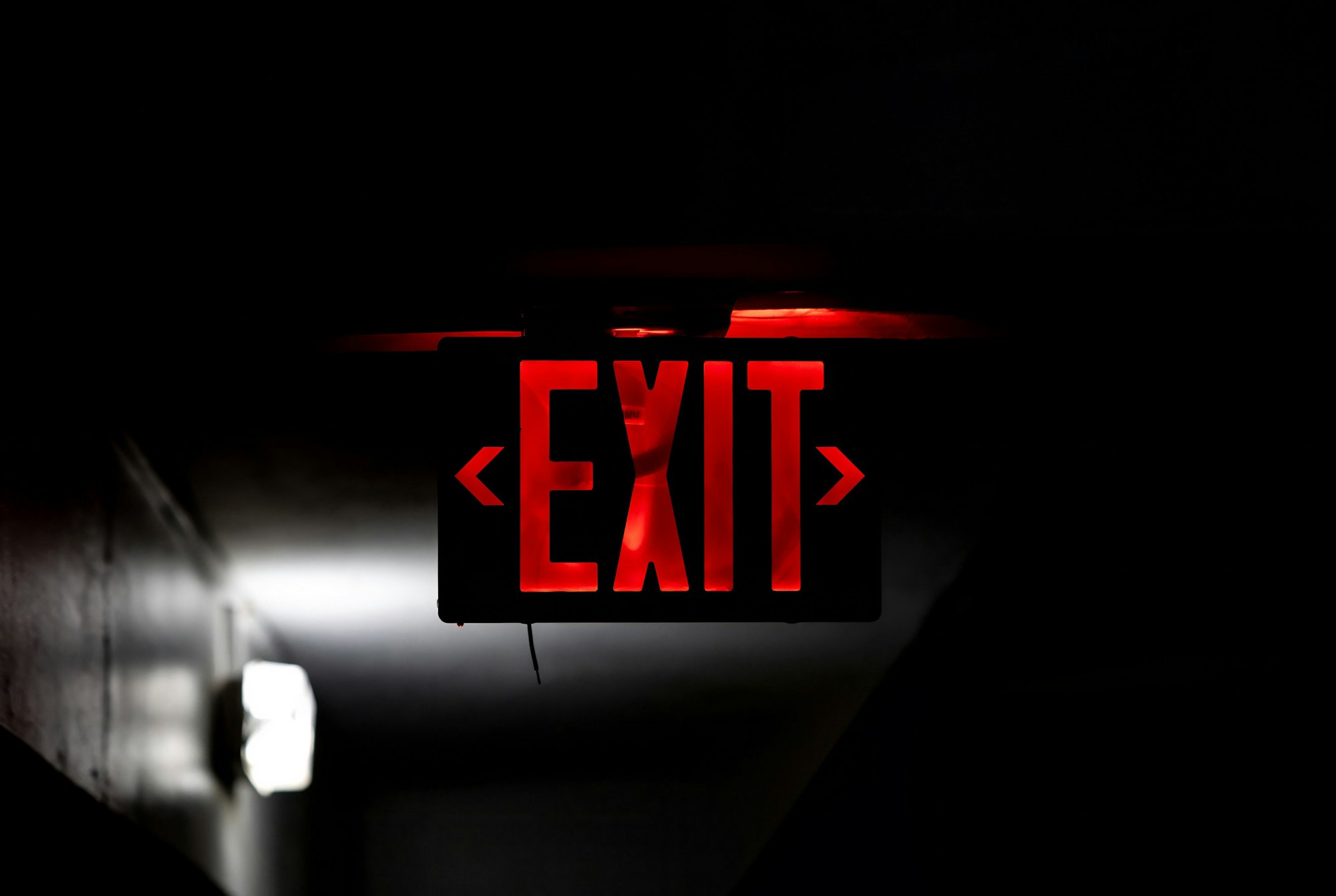 A glowing red exit sign hangs against a dark background, indicating the way out.