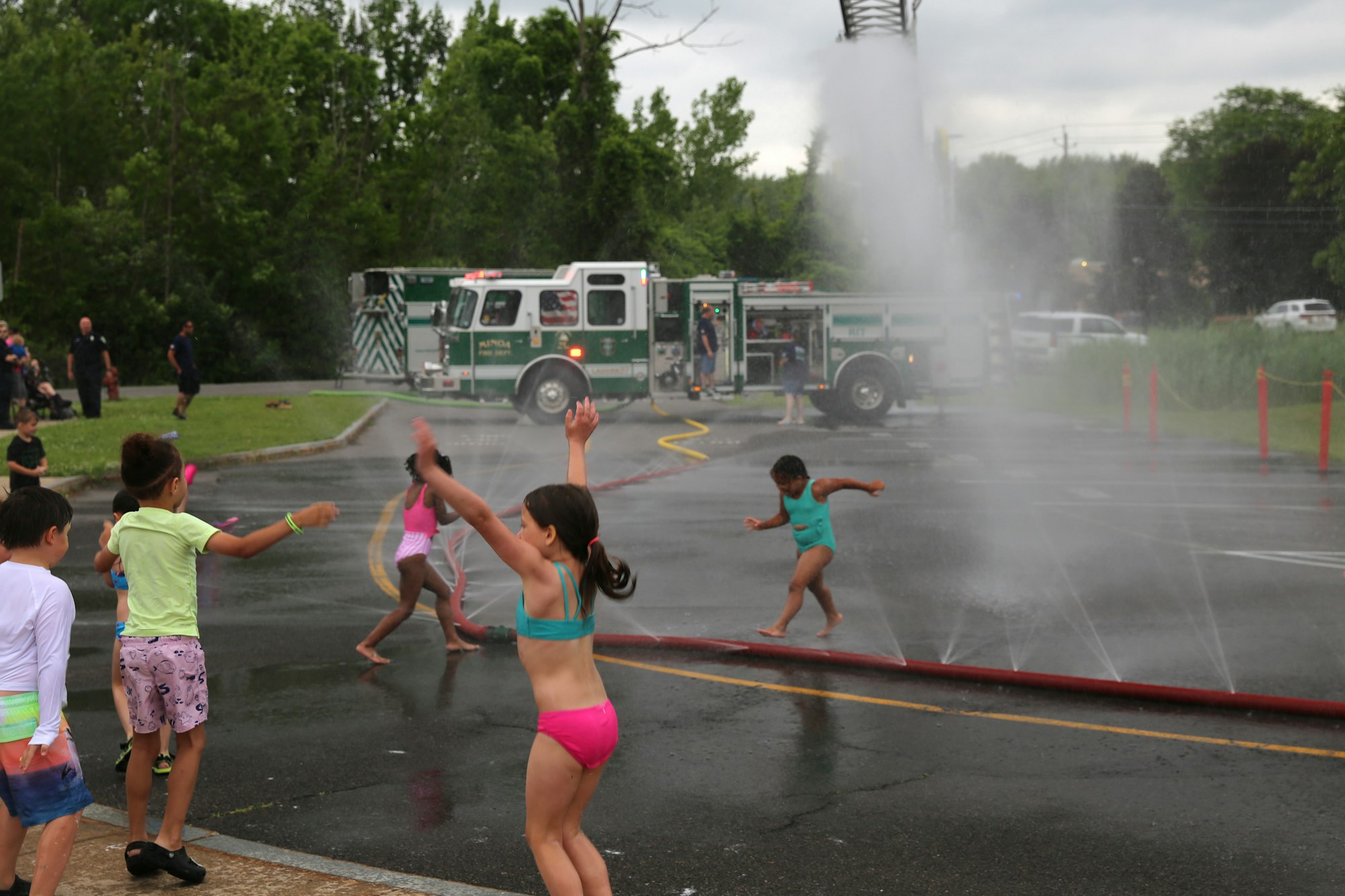 Children playing in water spray from a fire truck on a wet street.
