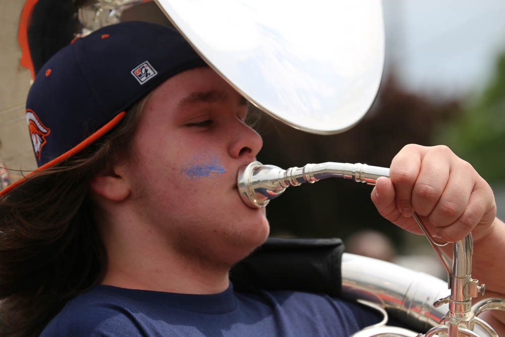 An ESM high school student, wearing a baseball cap, with face paint under his eyes, plays the tuba in the parade.
