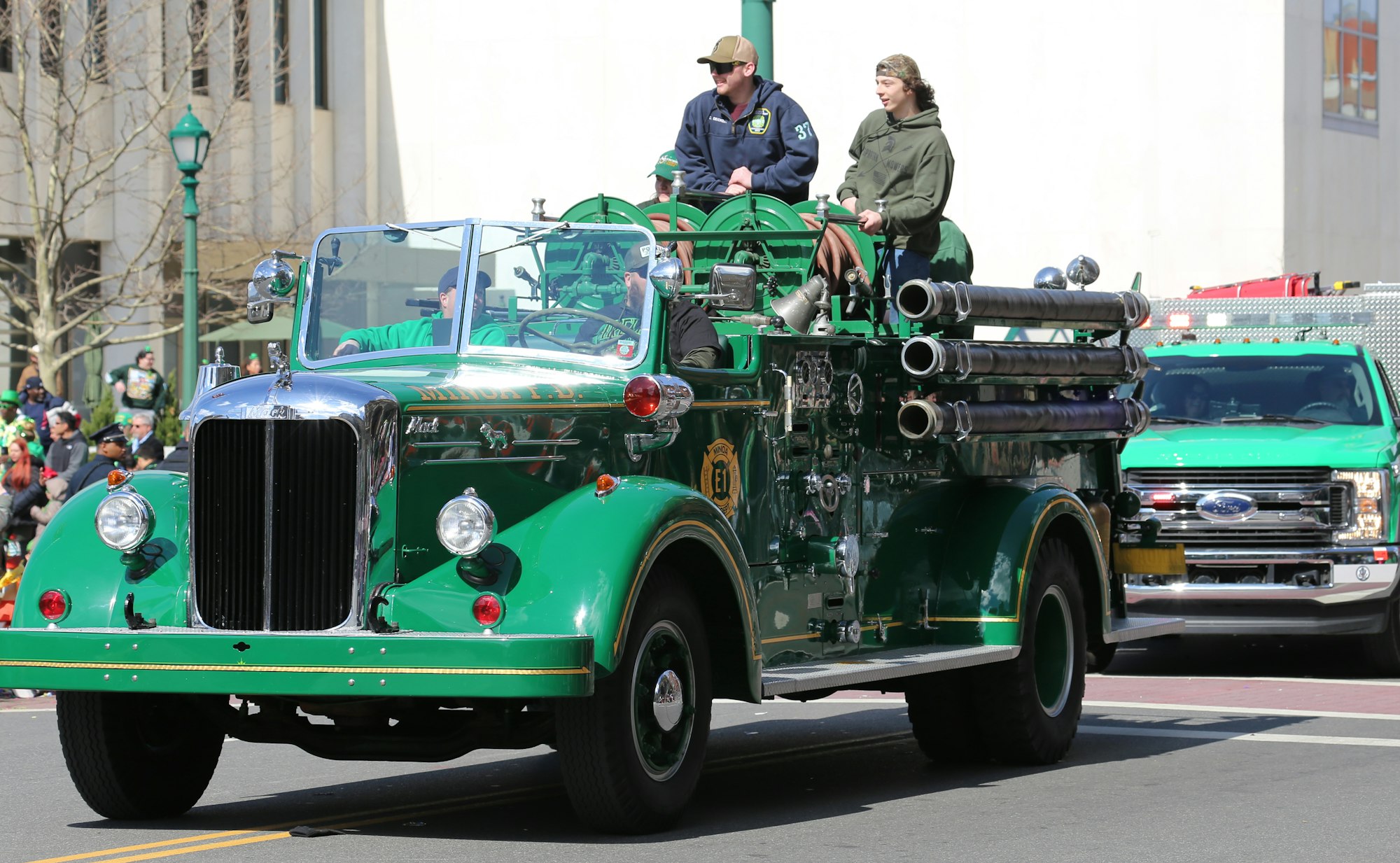 Vintage green firetruck with two people in a parade.