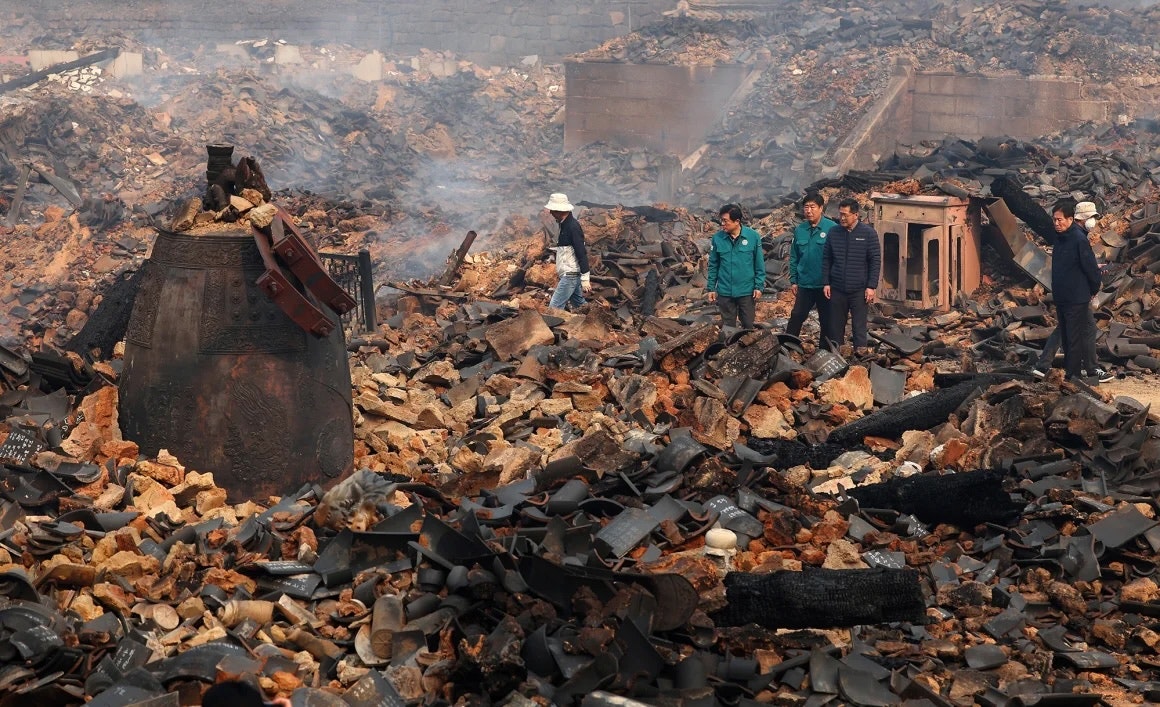 Debris and rubble from the burnt Gounsa Temple with people inspecting the damage.