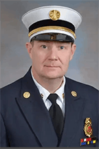 Shawn Tompkins in a fire chief uniform with badges and a white peaked cap.