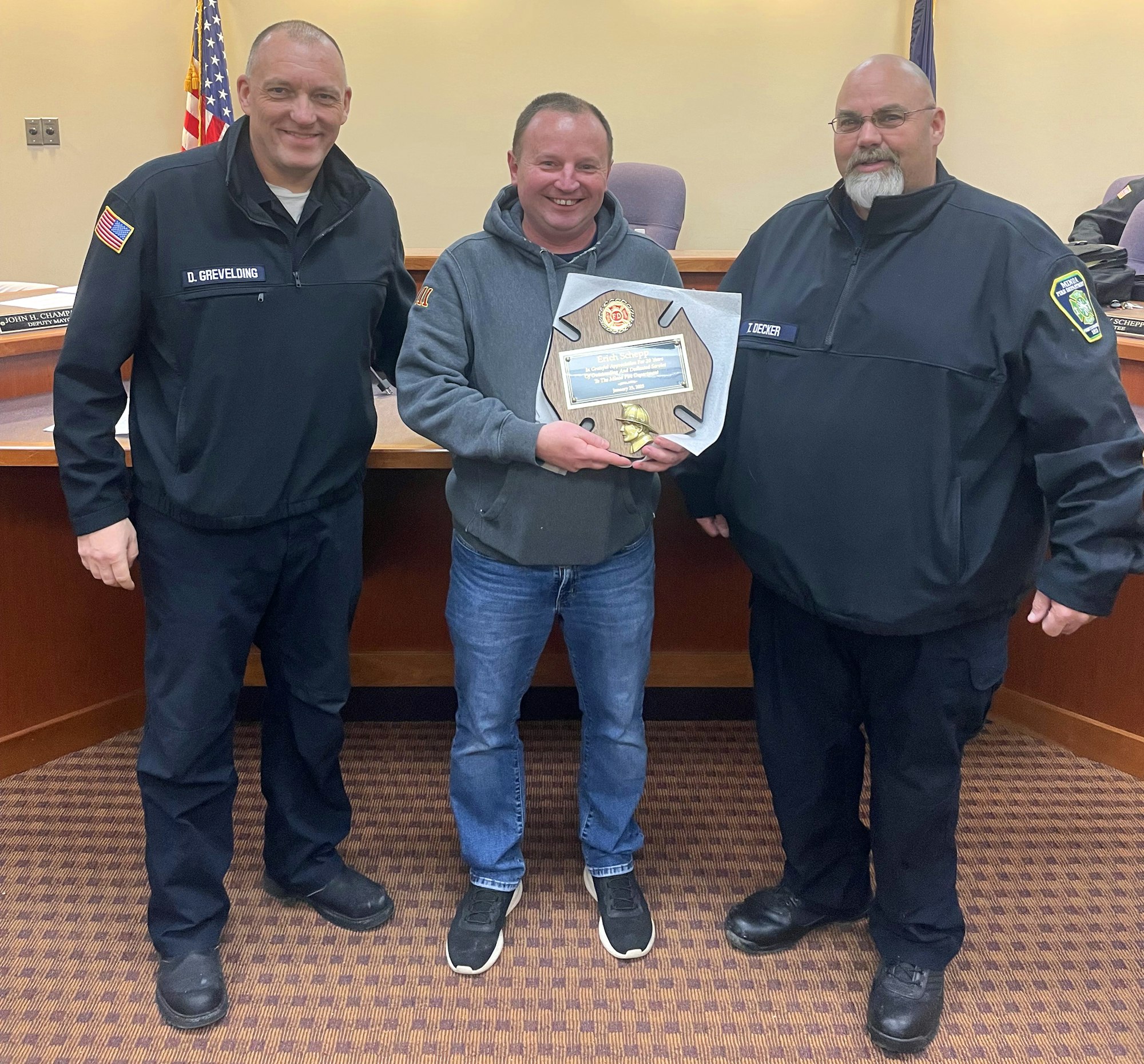 Chief Grevelding and President Decker flank Erich Schepp holding a firefighter-themed plaque.