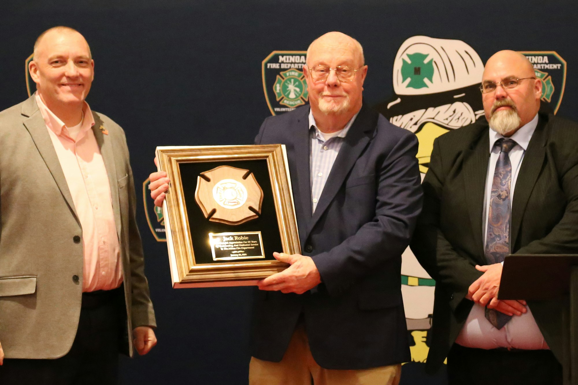 Chief Grevelding, Jack Robie (holding a framed award) standing in front of a backdrop with badges.