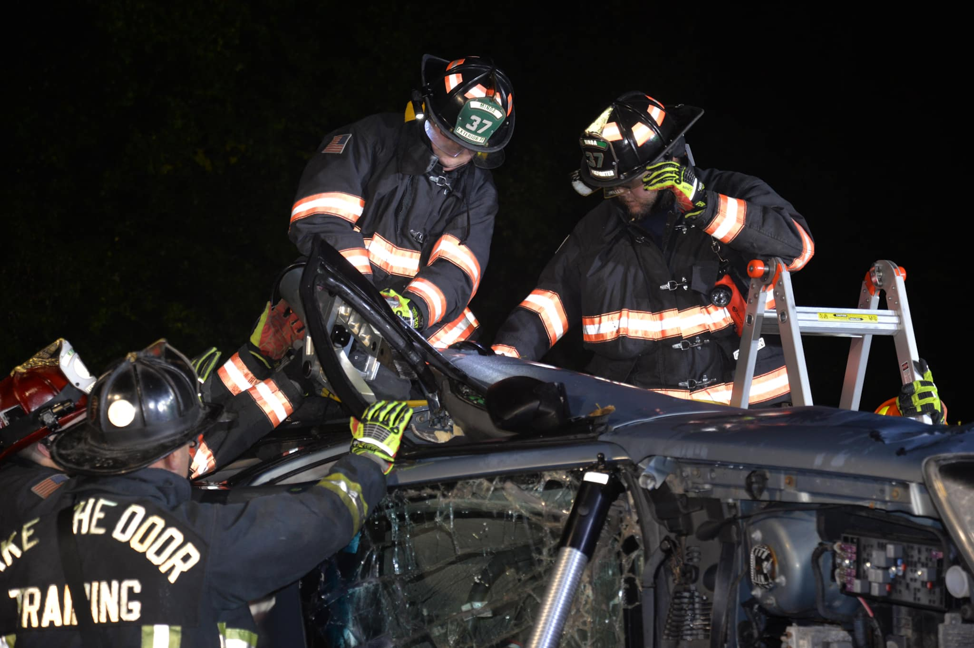 Firefighters using tools on a damaged vehicle, likely during a training exercise or rescue.