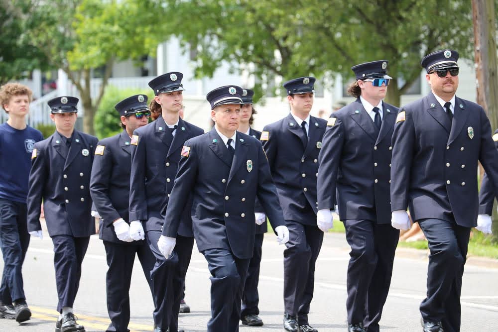 A group of uniformed firefighters is marching in a line, showcasing their discipline and dedication during a parade.