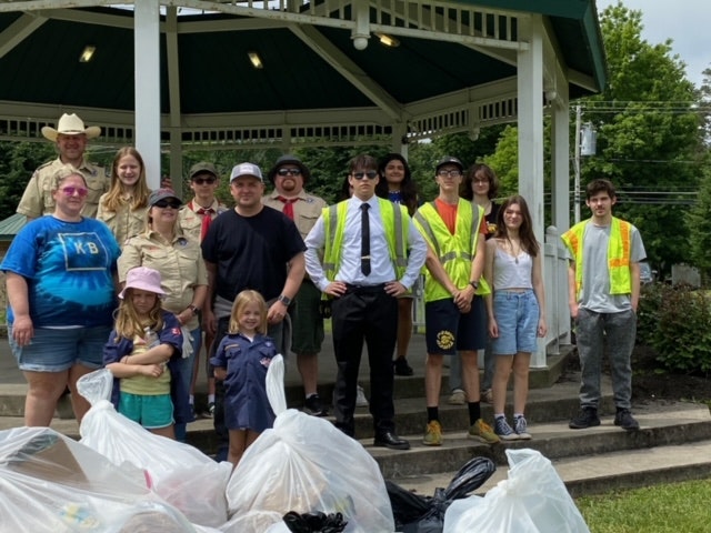 Alec stand in the center of a group of people near the gazebo in Lewis Park, with bags of collected trash, showing the success of the community clean-up event.