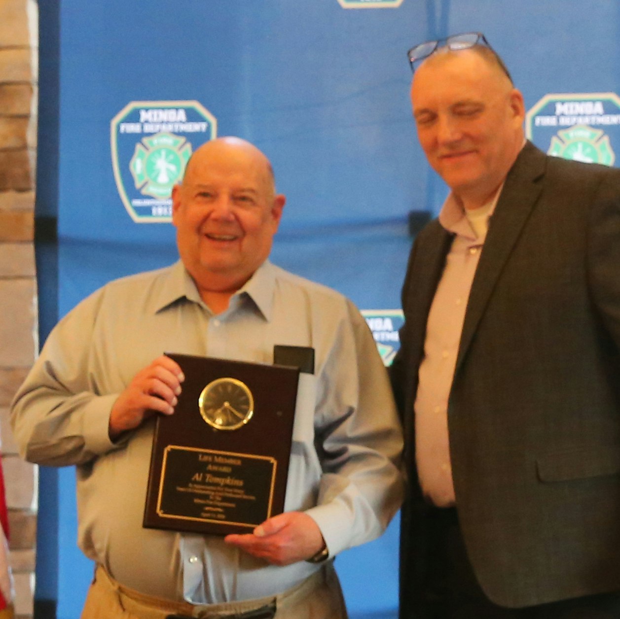 Two men pose for a photo at an event. One man holds an award plaque, while the other stands beside him, smiling.