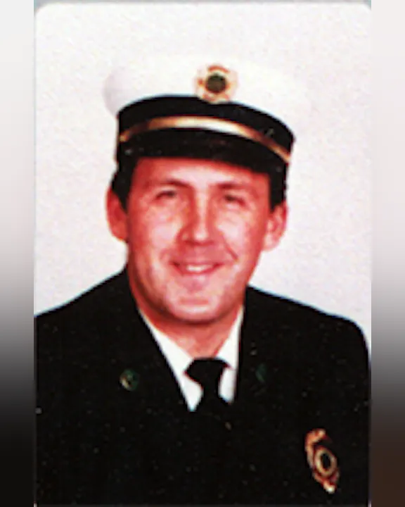 Lewell E. Troast, Jr., in a uniform and hat, fire department officer, smiling.