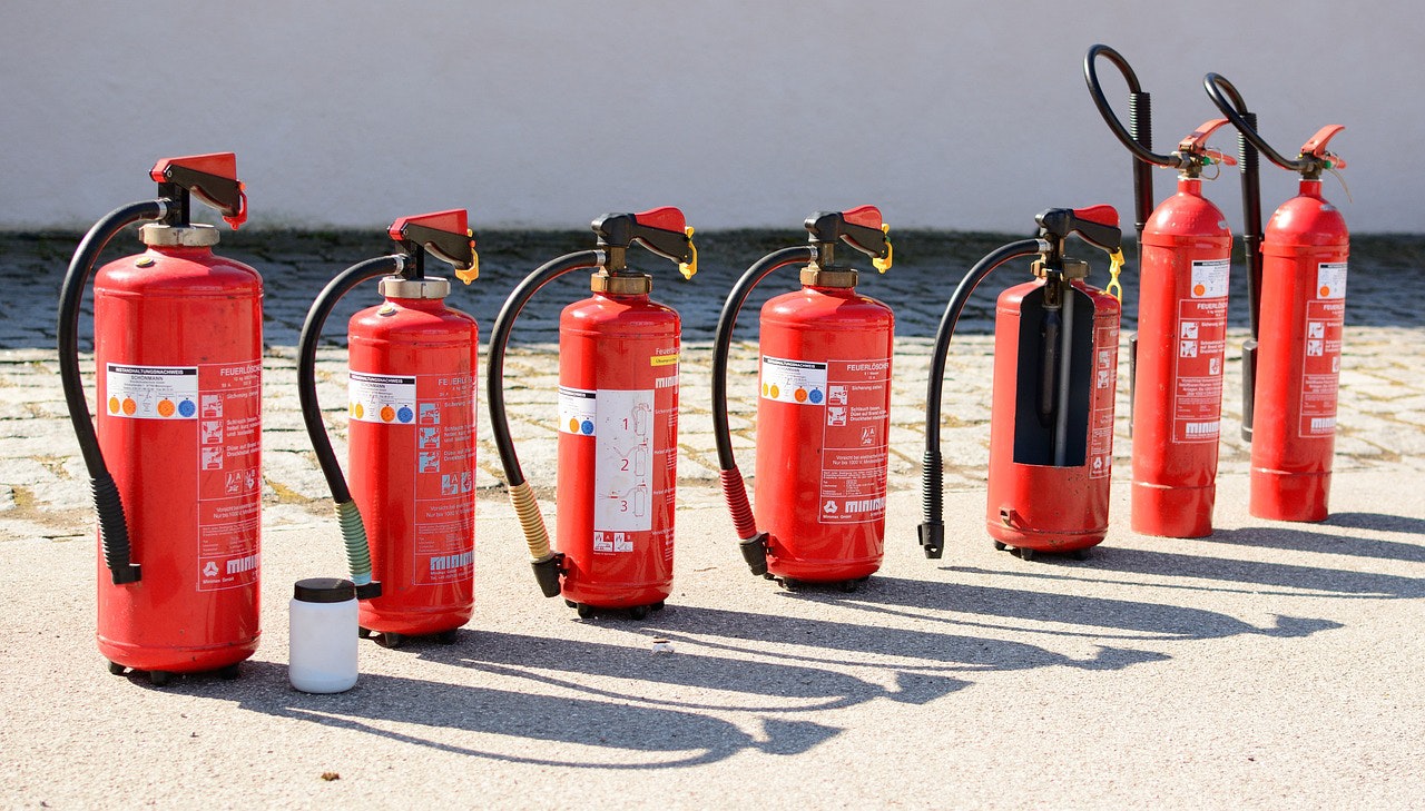 A row of red fire extinguishers lined up on a concrete floor, outdoors in daylight.