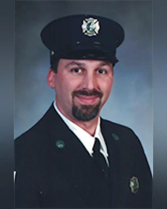 Todd Durantini in a dark uniform and hat, smiling at the camera against a plain background.