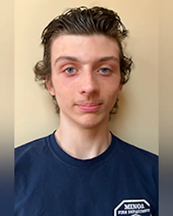 Kasey Marquart with short, wavy hair wearing a dark blue Minoa Fire Department t-shirt, standing against a plain background.