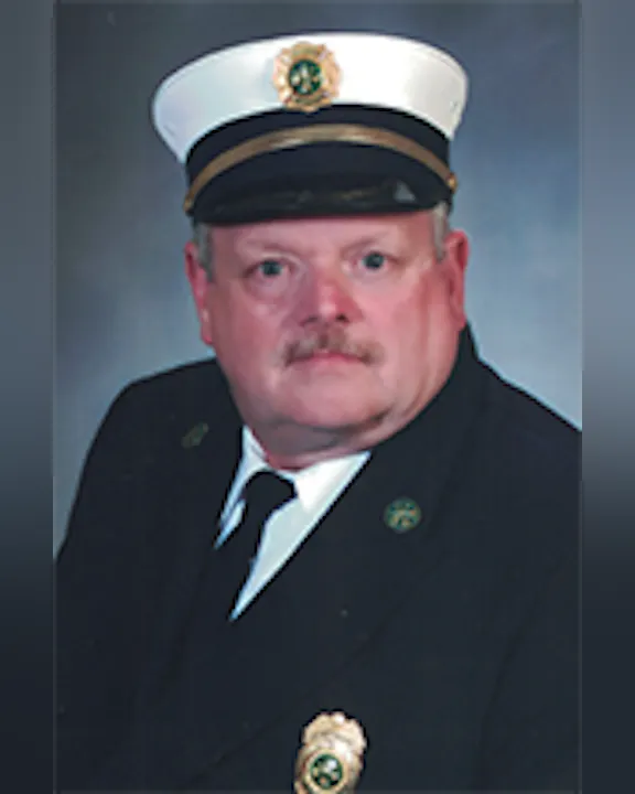 Dennis Erard in a formal uniform with a white hat and emblem, posing for a portrait.