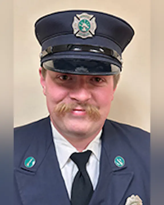 Ben Hess in a formal uniform with a hat, badges, and a mustache, smiling at the camera.