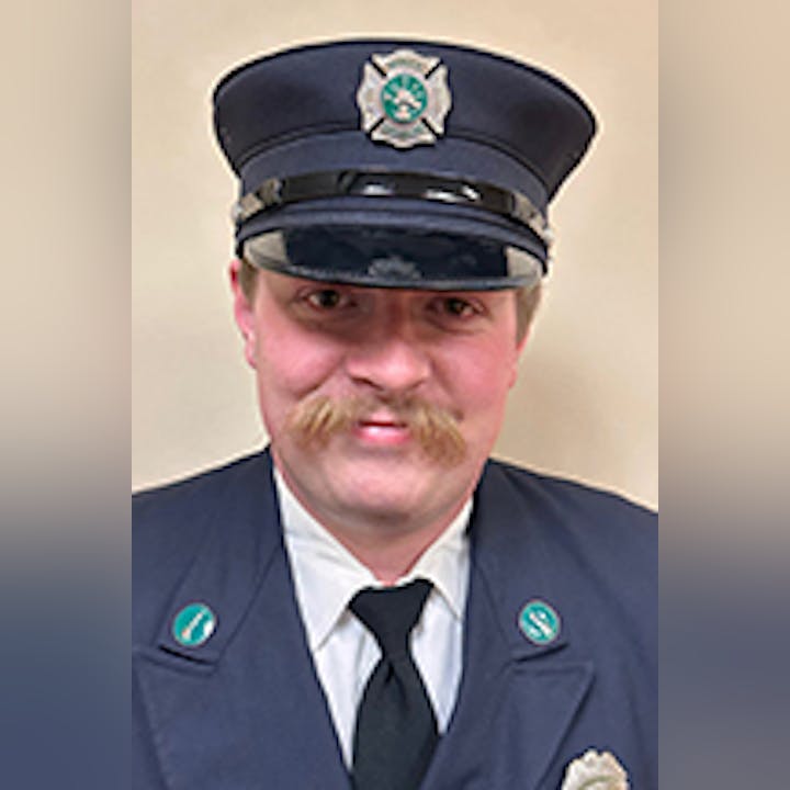 Ben Hess in a formal uniform with a hat, badges, and a mustache, smiling at the camera.