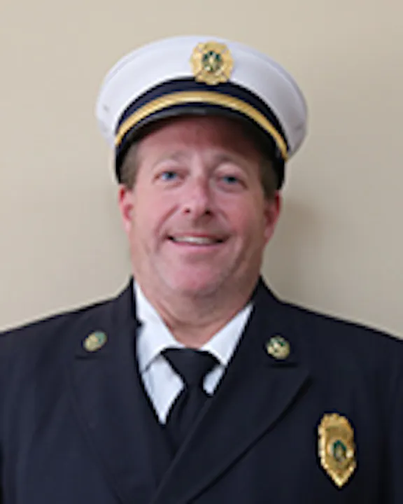 Dave Matthes in a formal firefighter uniform with a badge and a cap, smiling against a neutral background.