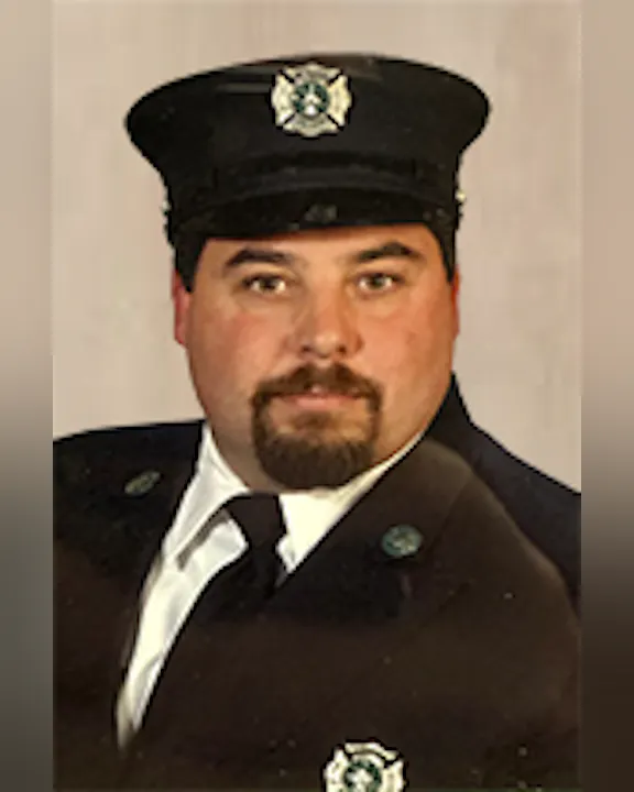 Chris Cretaro in a uniform with a peaked cap, representing a firefighter, looking confidently at the camera.