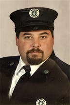 Chris Cretaro in a uniform with a peaked cap, representing a firefighter, looking confidently at the camera.