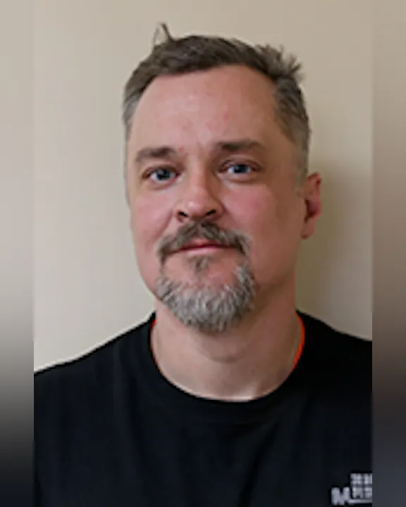 Jeremy Cunningham with short hair and a beard, wearing a black shirt, standing against a plain background.