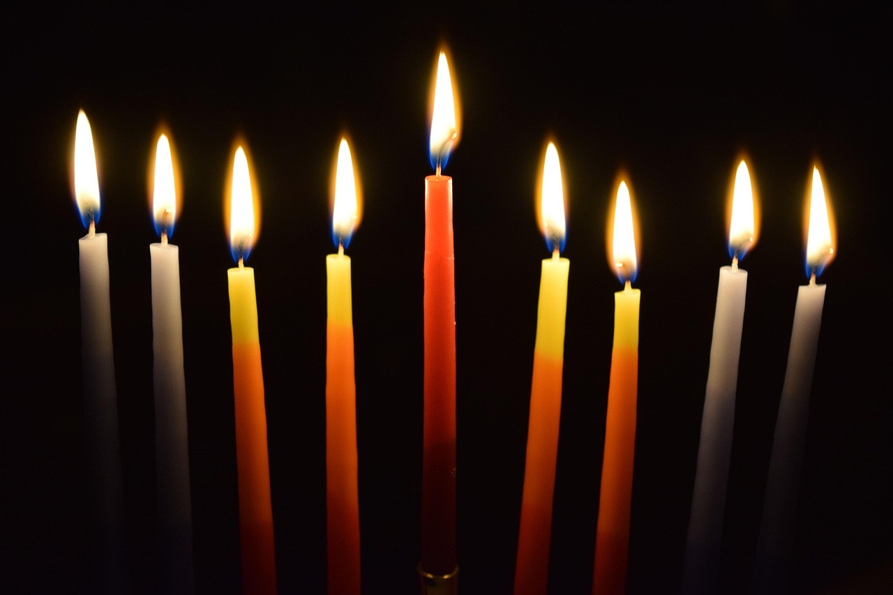 An arrangement of lit candles in varying colors against a dark background, creating a warm and inviting atmosphere.