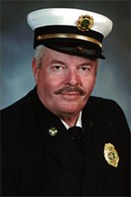 David Matthes, Sr. in a formal uniform with a white hat and badges, against a dark background.
