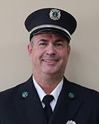 A smiling Ernie green in his uniform with a hat, standing against a beige background.