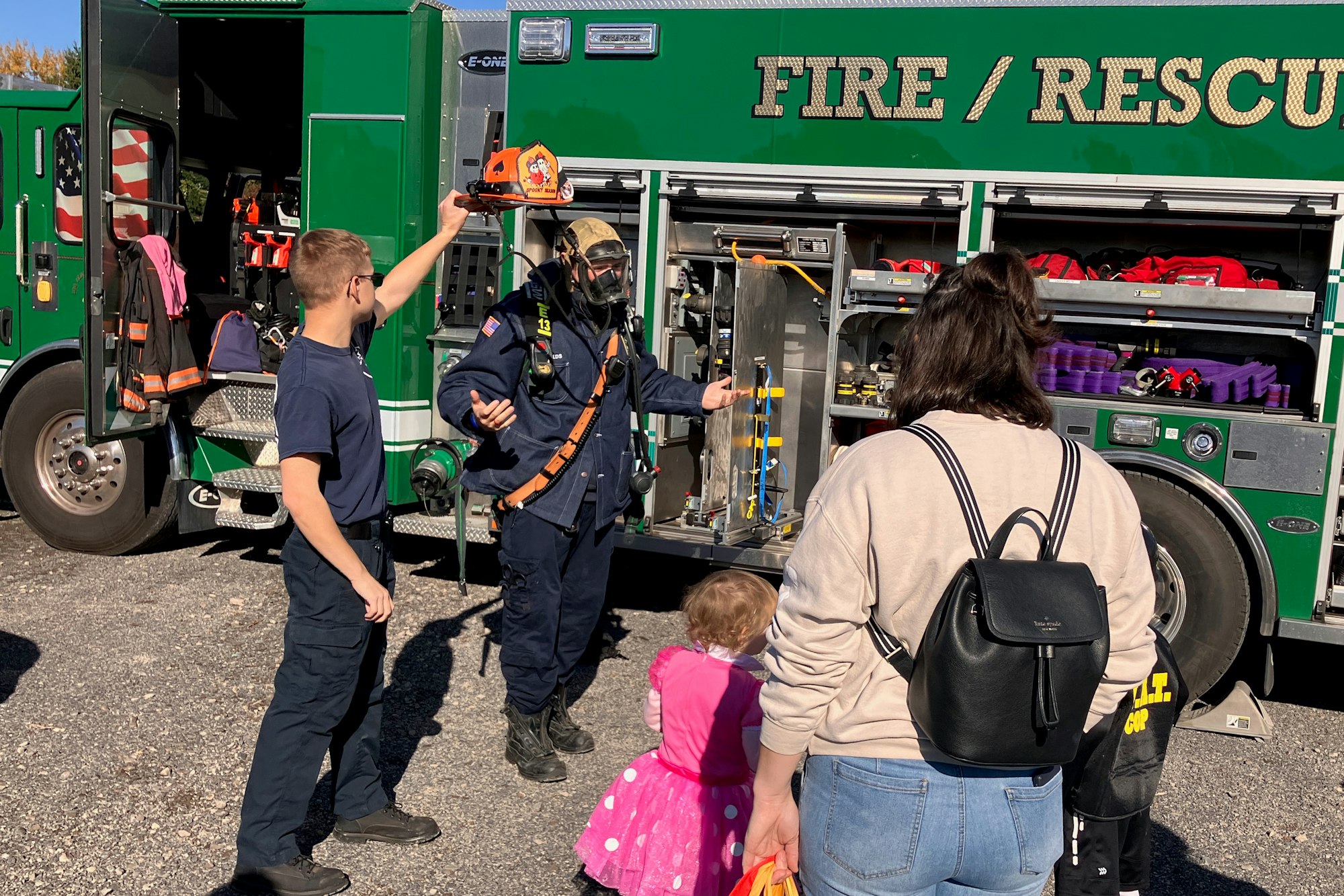 Firefighters showing equipment to a family by a firetruck.