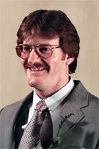 Gary Stoddard in 1984, wearing glasses, a suit, and a tie, smiling against a neutral background.