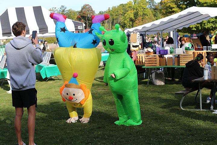 A person takes a photo of two people in inflatable costumes: an upside-down clown and a green alien, at the MitoAction outdoor event.