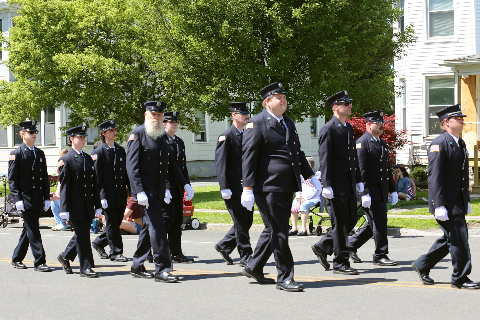 A group of people in uniform marching in a parade, with spectators sitting by the roadside.