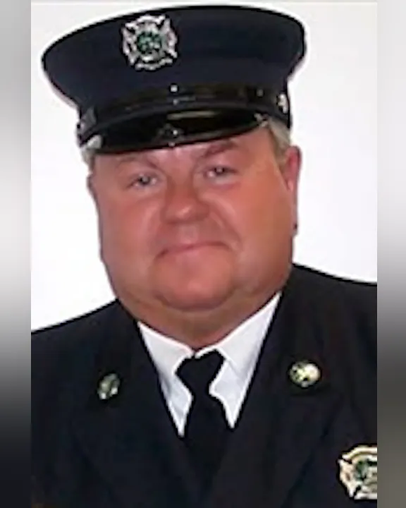 Marty Mullane in a firefighter uniform and cap, smiling.