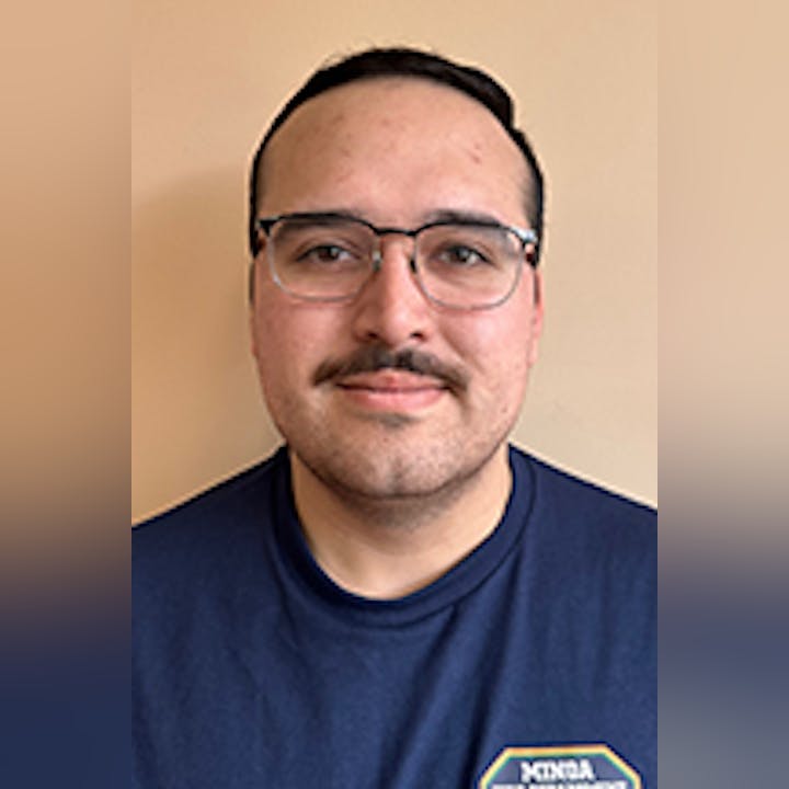Chris Dooher with glasses and a mustache, wearing a navy shirt, stands against a plain background.
