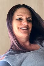 Dawn Andreiswith long hair, smiling slightly, and wearing a grey top. The background appears simple and neutral.