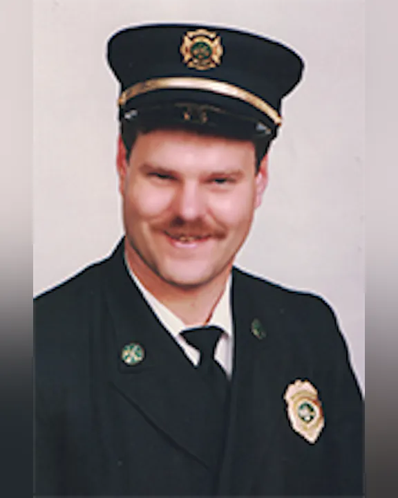 Mike Jarvis wearing a formal uniform with a cap, featuring badges and a tie, smiling at the camera.