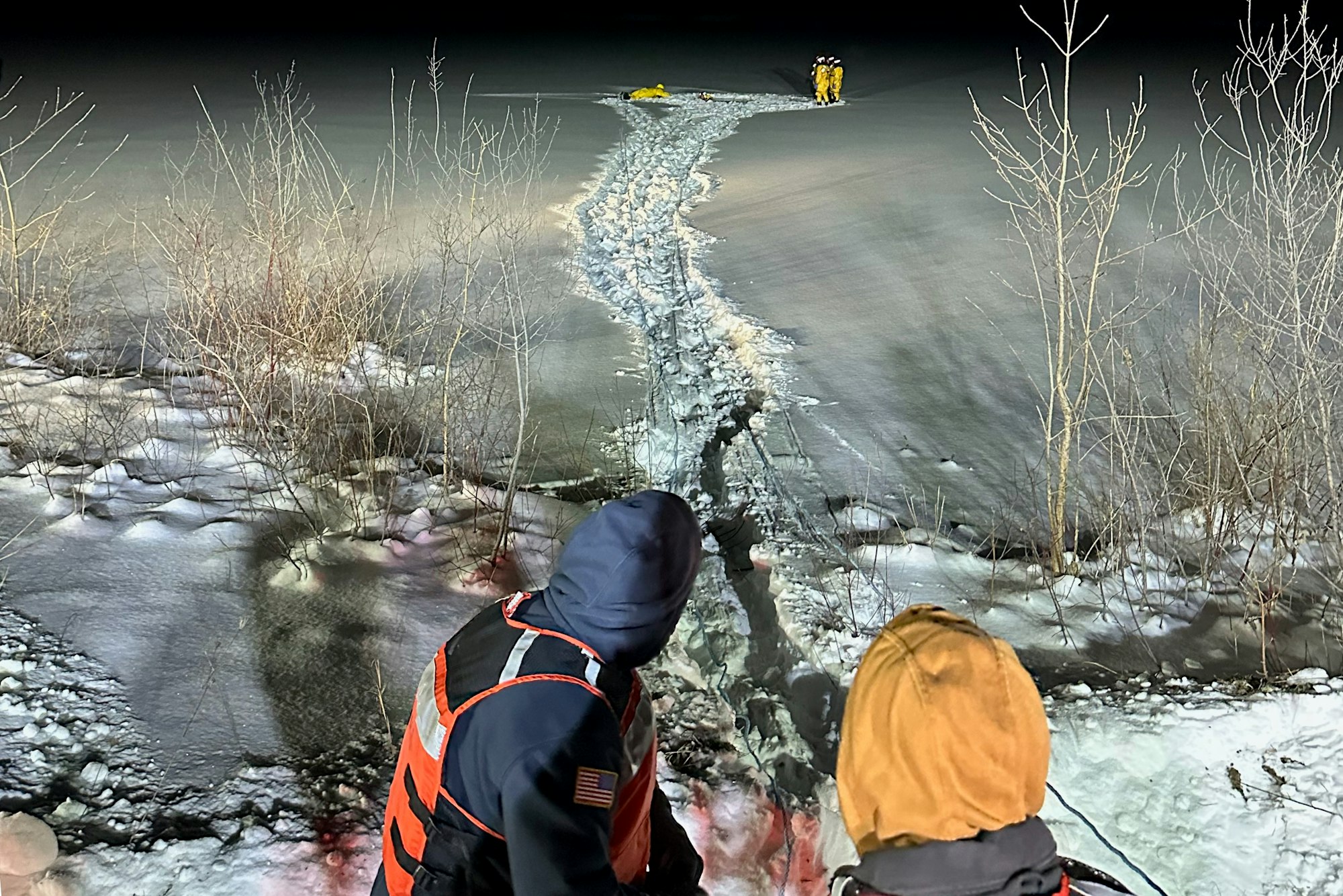 The image shows rescuers on ice at night, with a visible path through the snow and icy terrain, likely responding to an emergency.