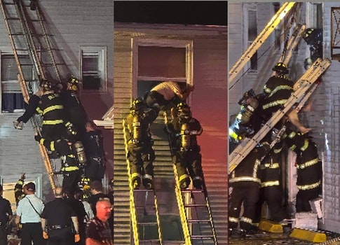 Firefighters rescue people using ladders at night next to a building.