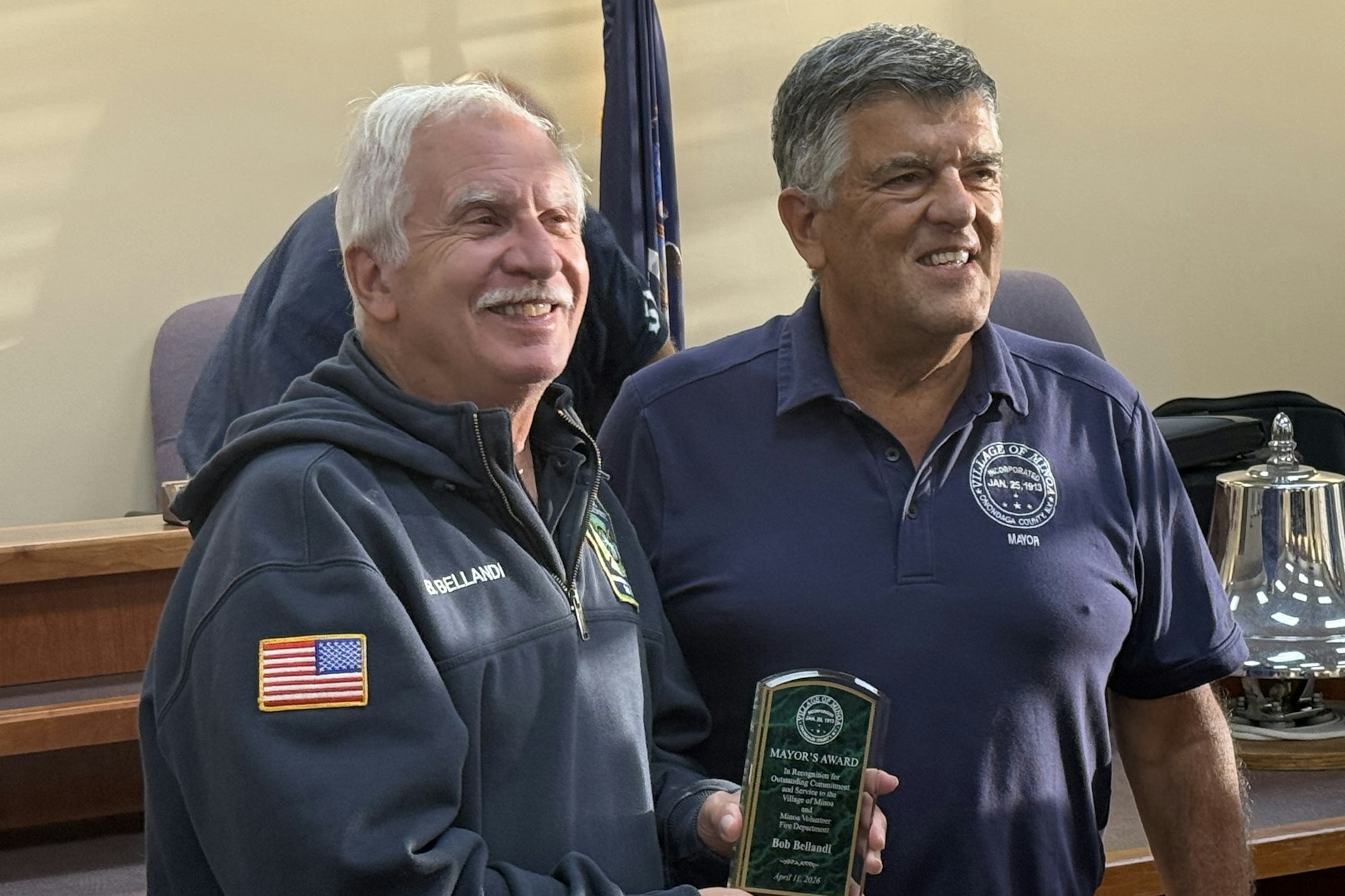 Bob Bellandi and Mayor Brazill stand smiling in a room, one holding a plaque for the Mayor's Award. The setting is the Minoa Board meeting room..