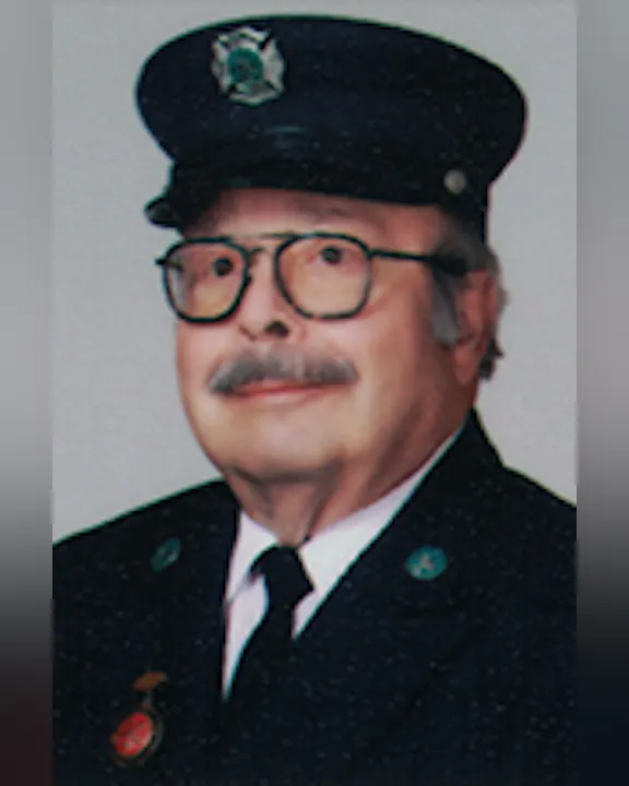 Ken D'Angelo in a uniform with glasses and a cap, smiling slightly.