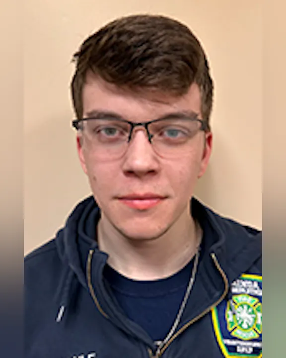 Austin Maule with glasses wearing a jacket, standing against a plain background.