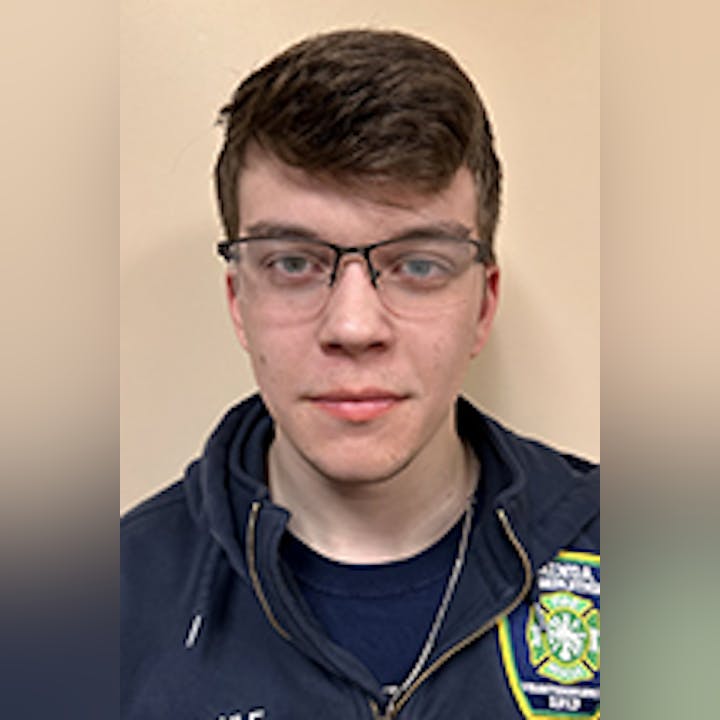 Austin Maule with glasses wearing a jacket, standing against a plain background.