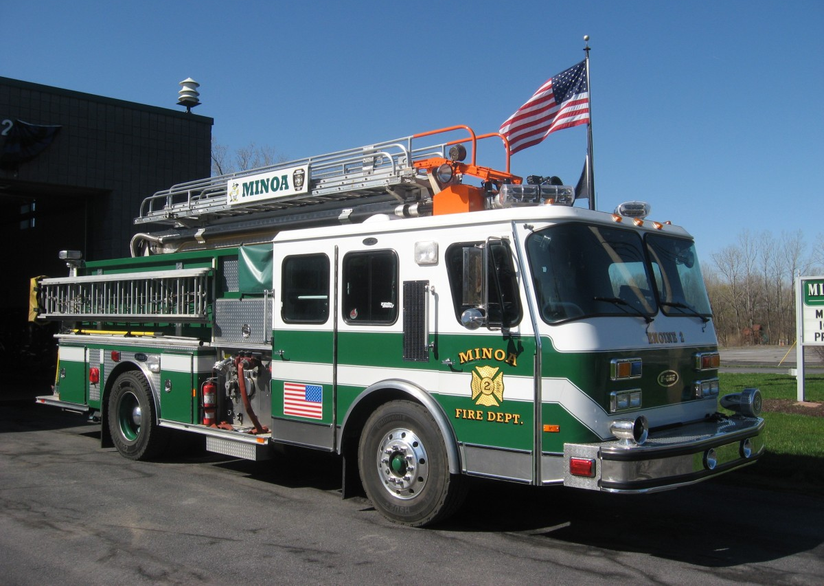 A firetruck with the American flag atop it, outside a fire station.