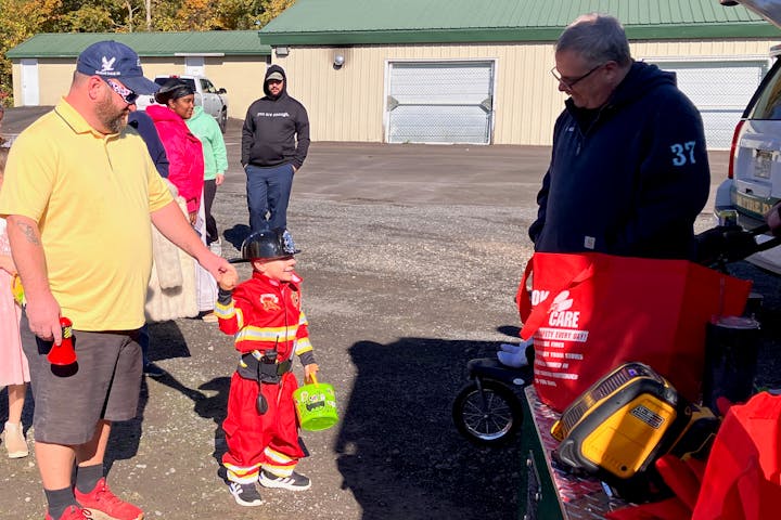 A child in firefighter costume with adults at the 2024 Trunk and Treat in Lewis Park