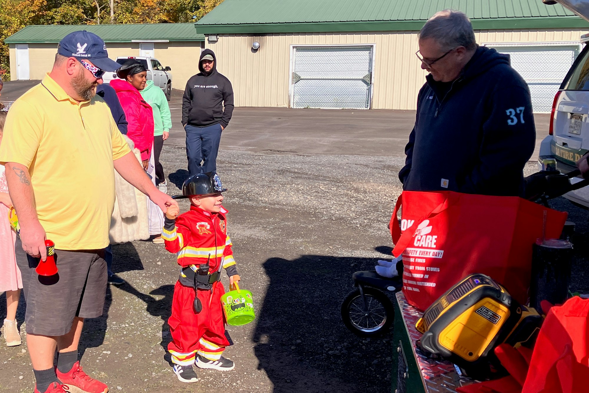 A child in firefighter costume with adults at the 2024 Trunk and Treat in Lewis Park