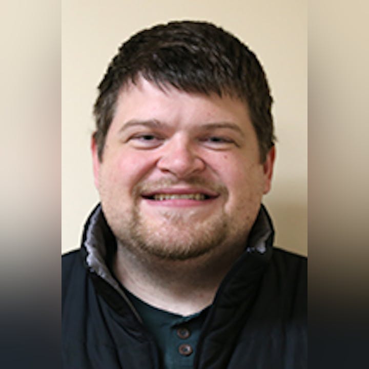 A smiling Josiah Roloson with a black jacket and collar shirt against a light background.