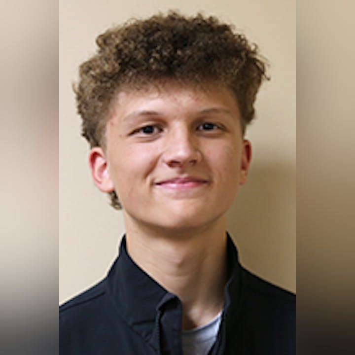 Brayden Maylone with curly hair wearing a dark jacket, smiling against a plain background.