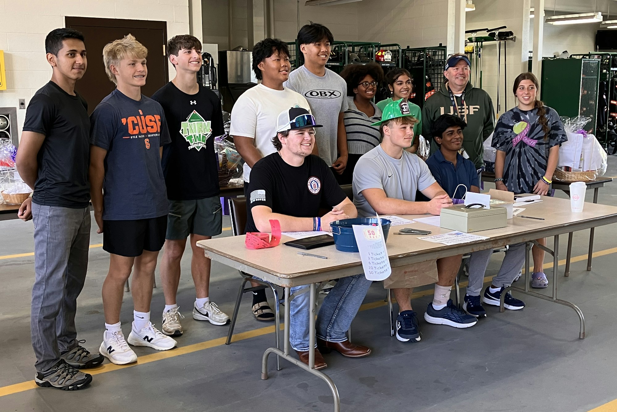 A group of cheerful DECA students standing and sitting behind a table, for the fundraiser.