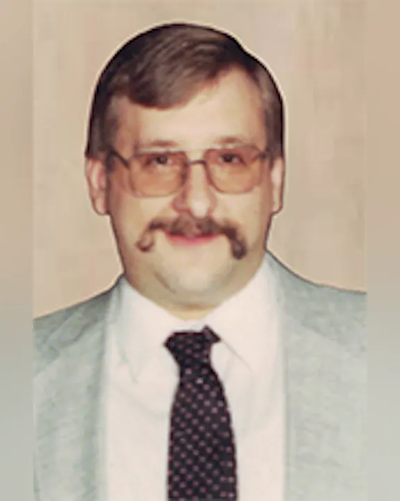 Dave Billy with glasses, mustache, and a light-colored suit with a dark polka dot tie.