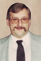 Dave Billy with glasses, mustache, and a light-colored suit with a dark polka dot tie.